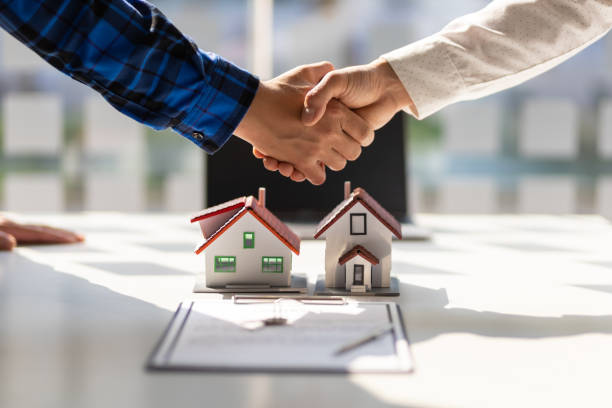 Handshake between two people over a real estate agreement, with small house models on the table in the foreground